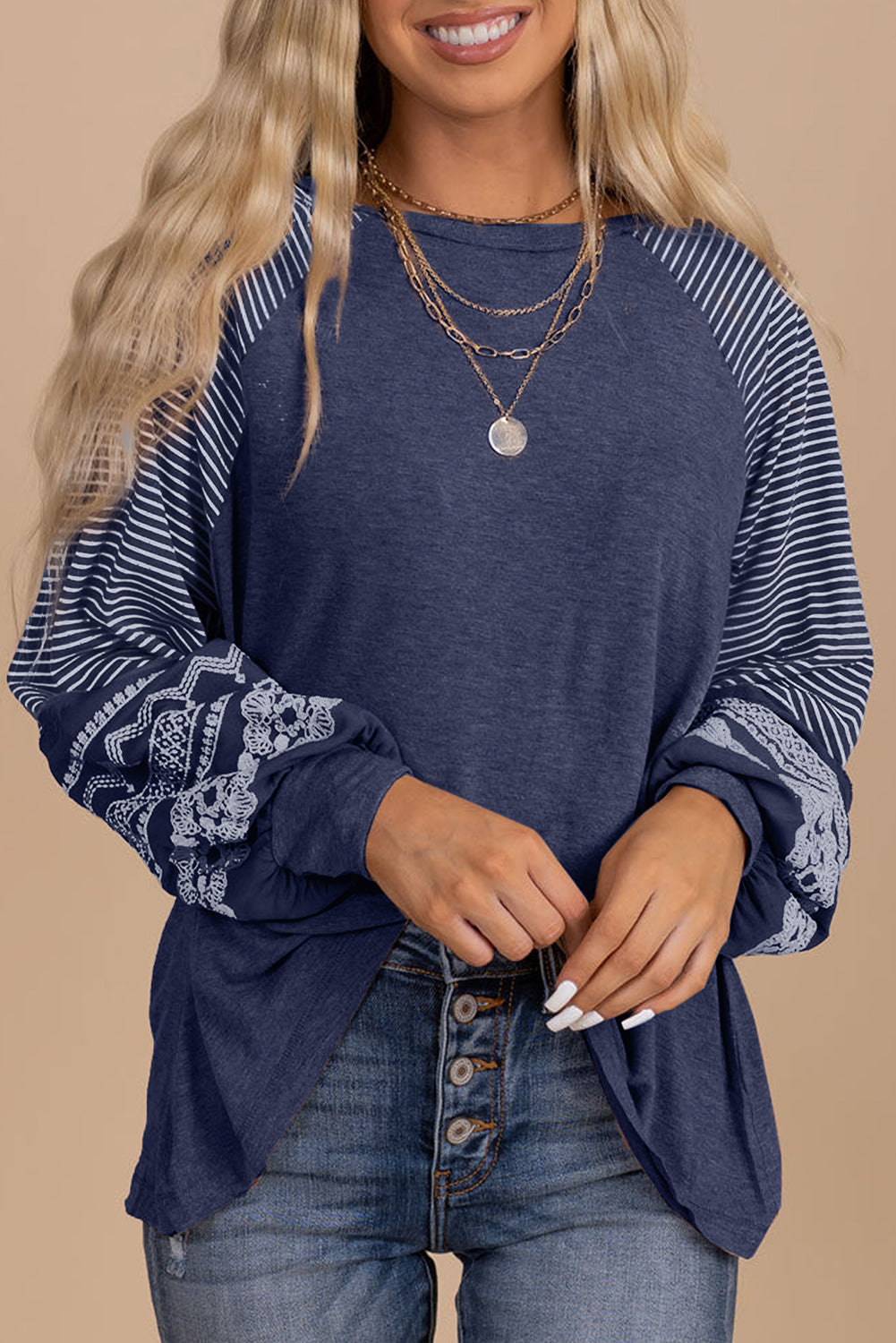 Woman wearing a blue long-sleeve top with patterned sleeves on a beige background