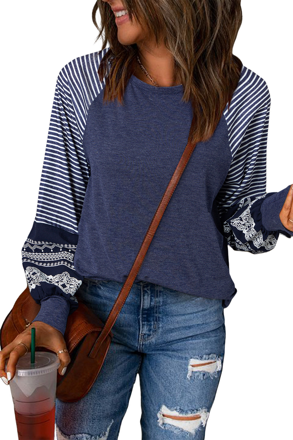 Woman wearing a blue and white striped long-sleeve top with ripped jeans, holding a drink.