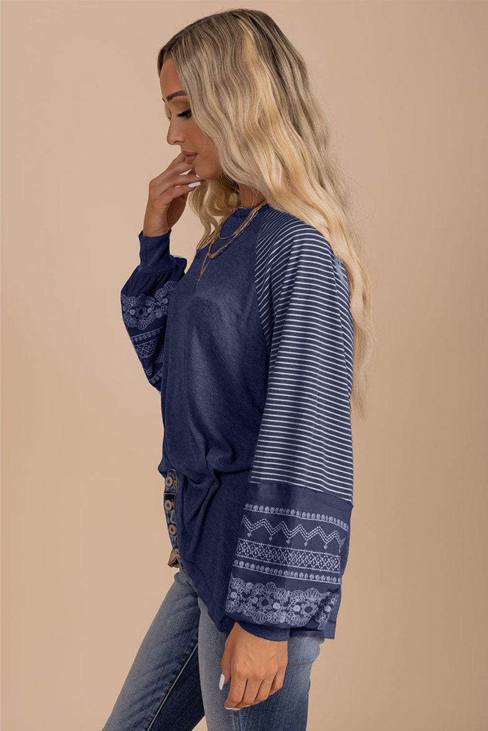 Woman wearing a navy blue long-sleeve top with intricate patterns on a beige background