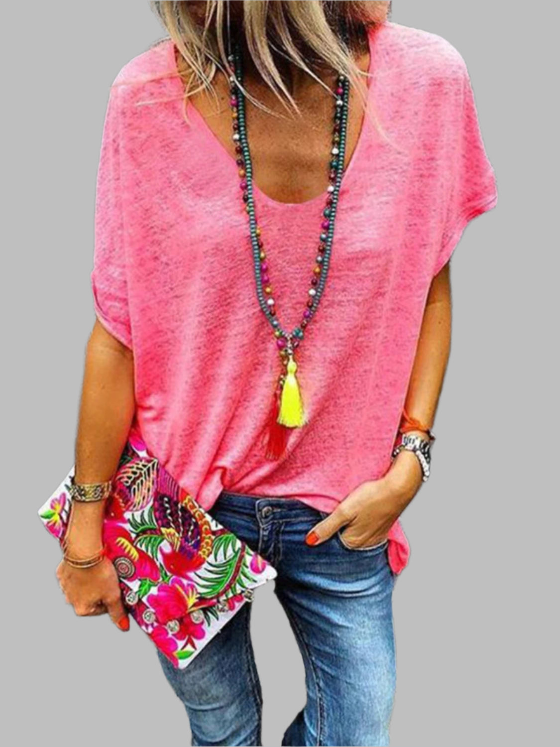 Woman wearing a boho-chic style t-shirt top with a scoop neck and short sleeves. Loose fitting t-shirt in pink, boho necklace, and boho clutch.