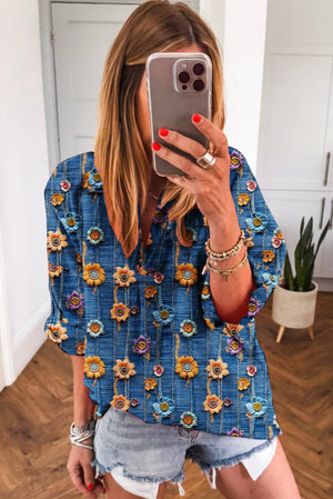 Person wearing a blue floral blouse taking a mirror selfie.