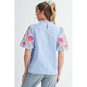 Woman wearing a blue checkered top with floral sleeves on a white background