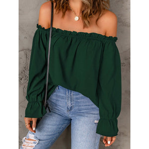 Green off-shoulder top worn by a person against a gray concrete wall.
