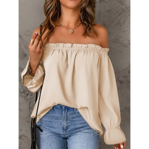 Woman wearing a beige off-shoulder top and blue jeans against a gray background