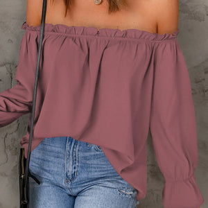 Person wearing a mauve off-shoulder top and blue jeans against a gray background