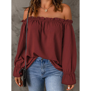 Woman wearing a burgundy off-shoulder top and blue jeans against a gray background