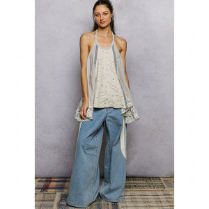 Woman wearing a layered outfit with a top, vest, and jeans against a plain background