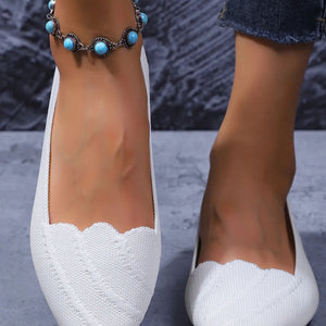 White shoes with scalloped edges worn by a person, with a blurred background.