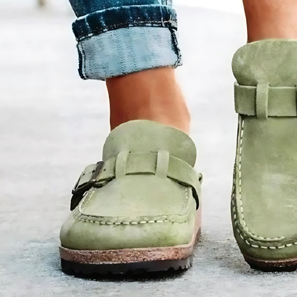 Green suede shoes with buckles worn by a person on a light background