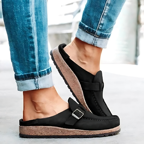 Black sandals with cork soles worn with blue jeans on a light background