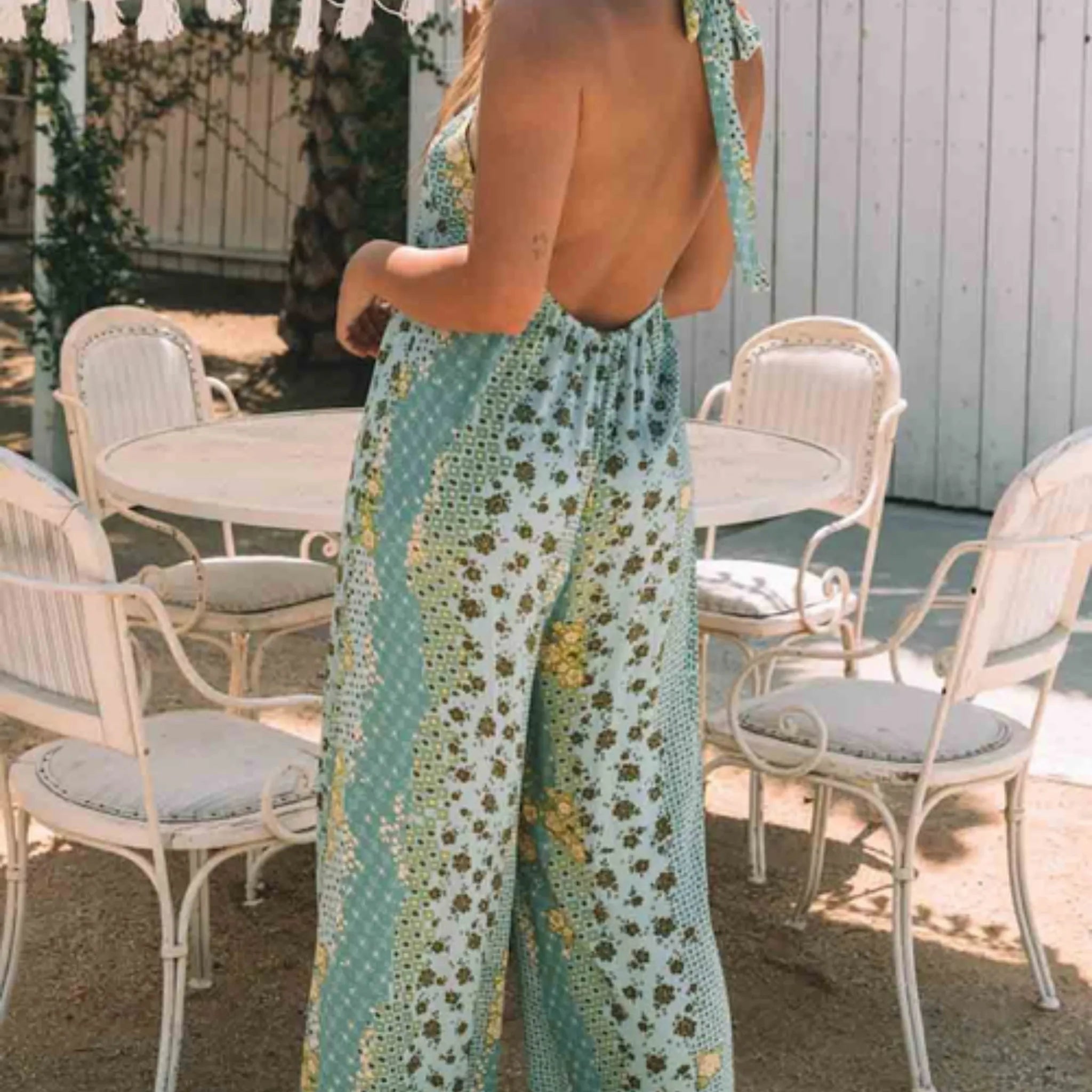 Person wearing a green floral dress standing in an outdoor setting with chairs and tables.