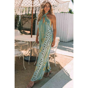 Woman in a green patterned dress standing outdoors near a table and chairs.