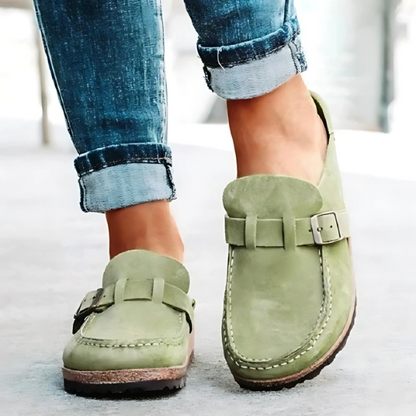 Green loafers with buckles worn with rolled-up jeans on a light background