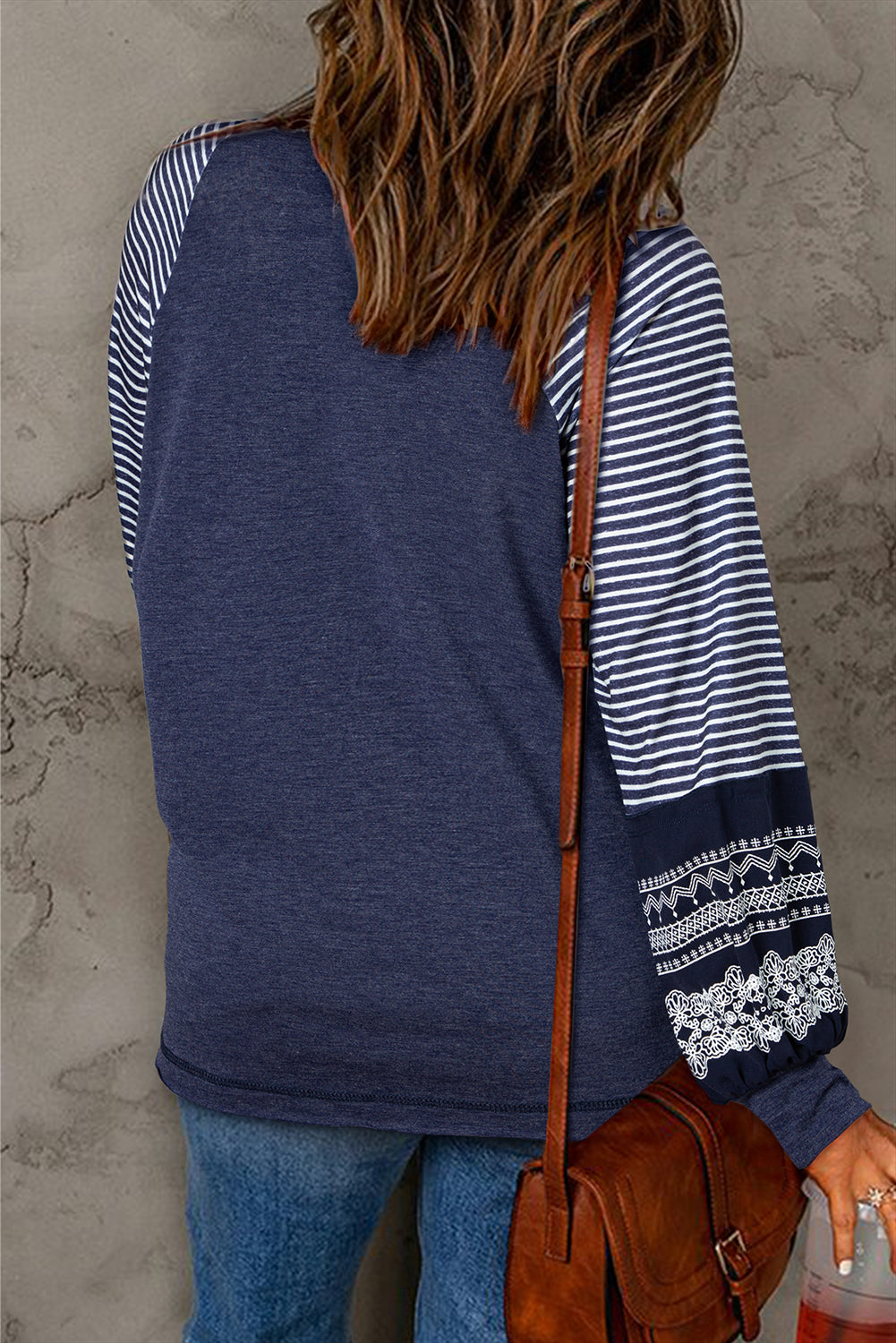 Person wearing a blue and white striped long-sleeve shirt with lace details, holding a brown leather bag.