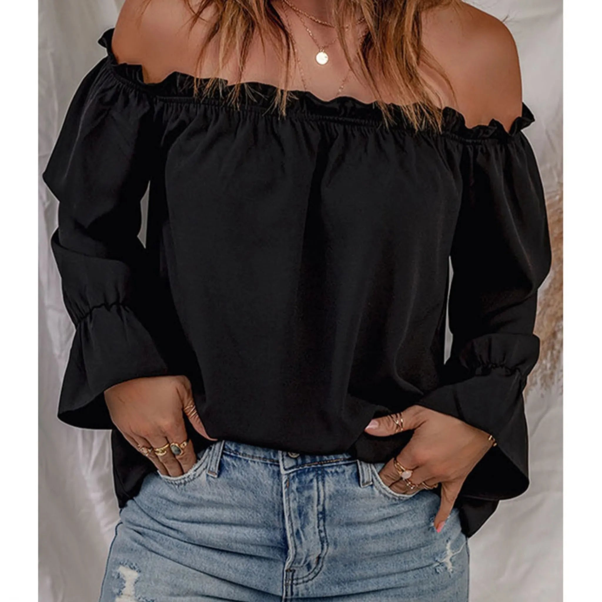 Person wearing a black off-shoulder top and blue jeans against a neutral background