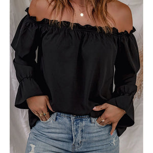 Person wearing a black off-shoulder top and blue jeans against a neutral background