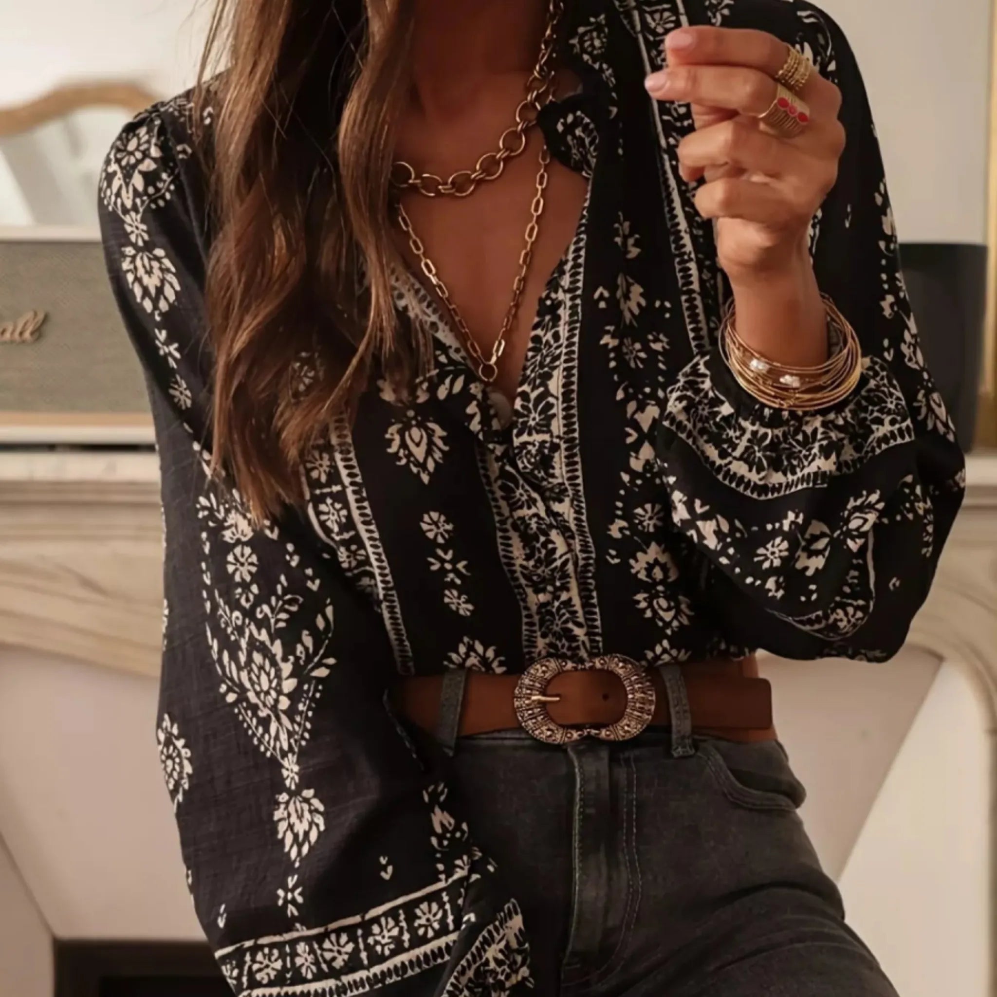 Person wearing a black and white patterned blouse with a brown belt and jewelry.
