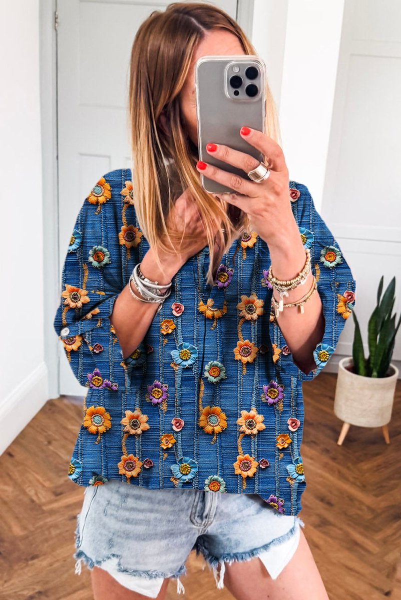 Woman taking a mirror selfie wearing a blue floral top and denim shorts.