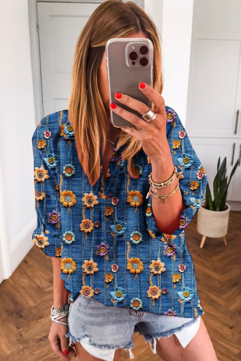 Person wearing a blue floral blouse taking a mirror selfie.