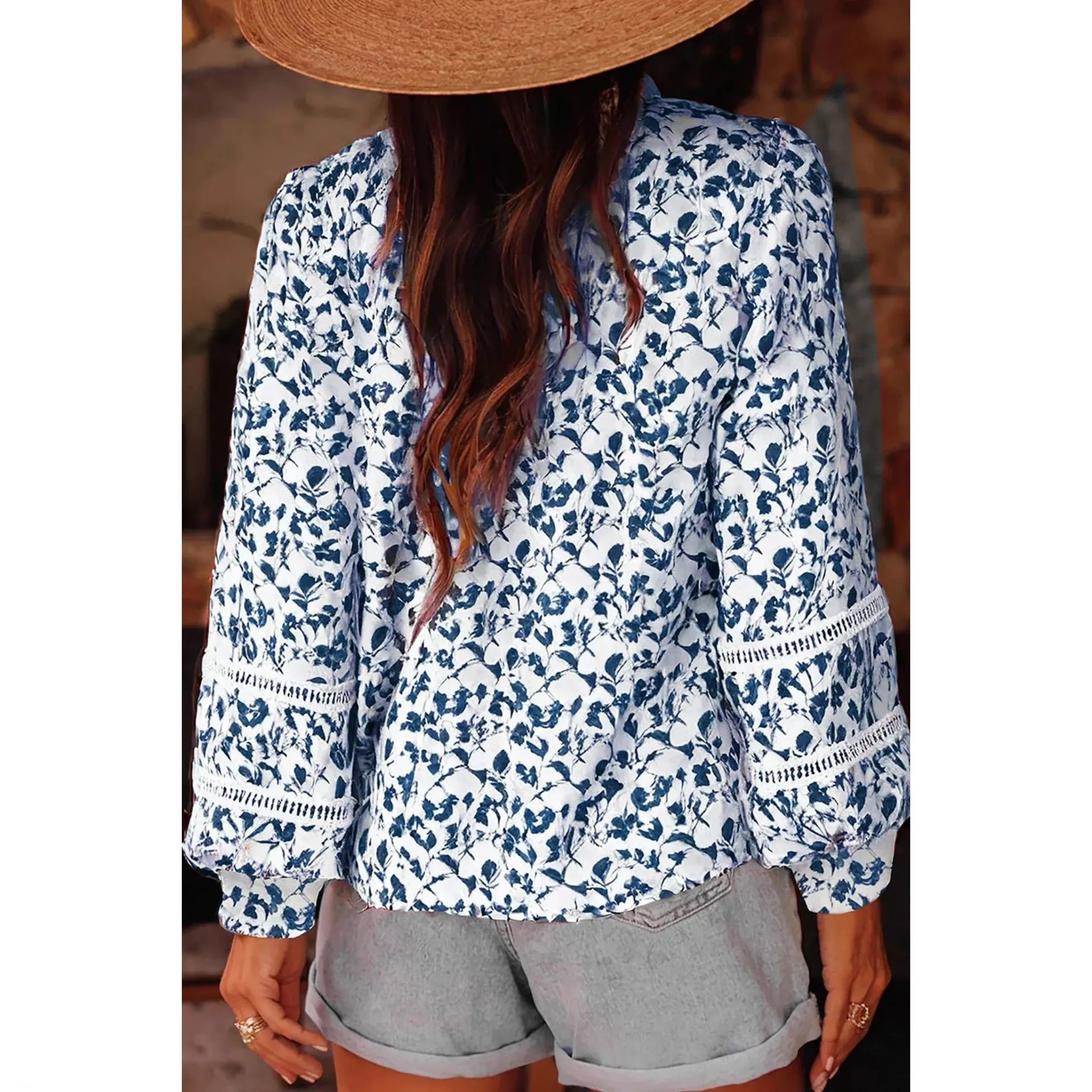 Person wearing a blue floral blouse with long sleeves and gray shorts, partially obscured by a straw hat.