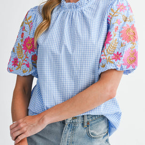 Blue checkered blouse with floral embroidery on sleeves and neckline, paired with jeans.