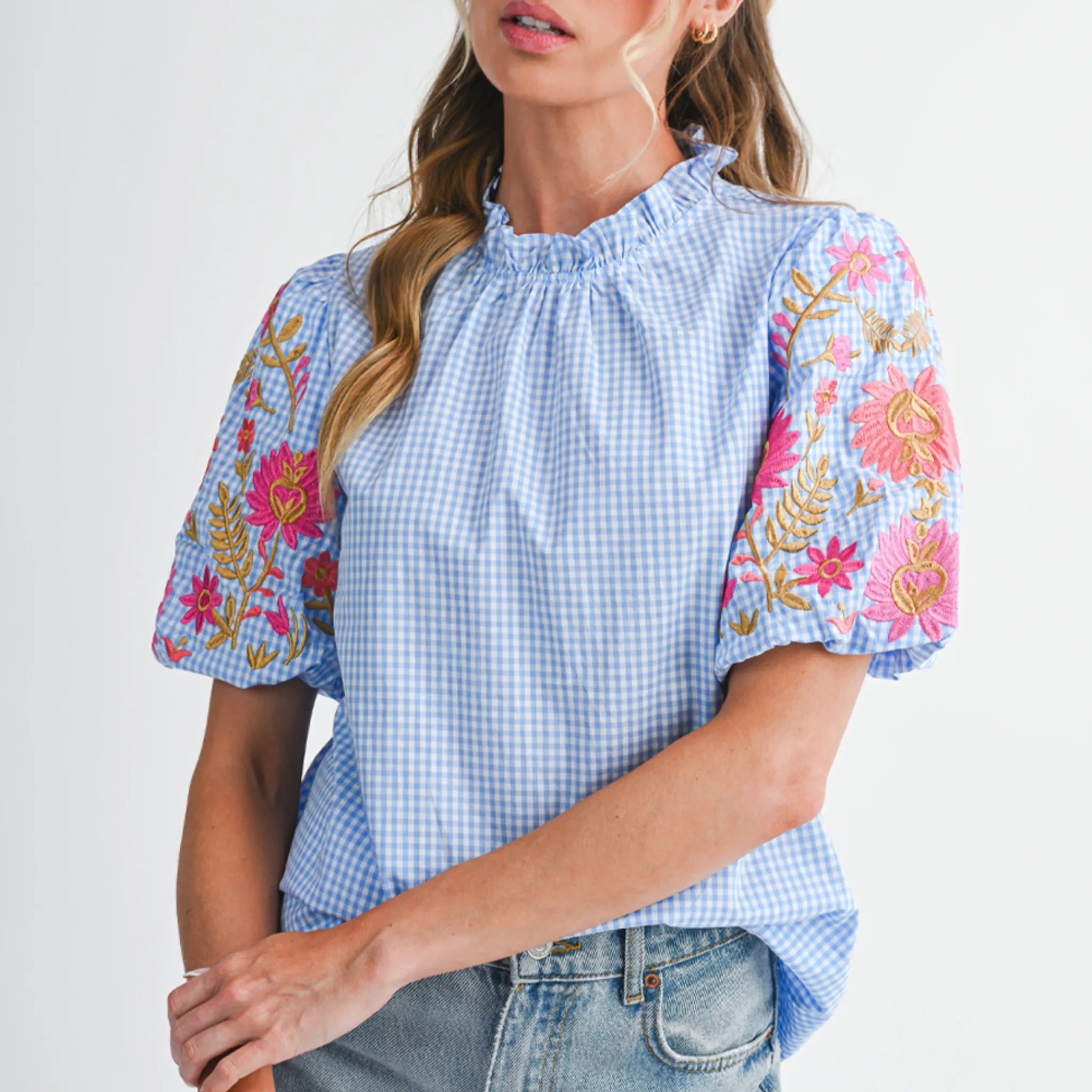 Woman wearing a blue checkered blouse with floral embroidery on a white background