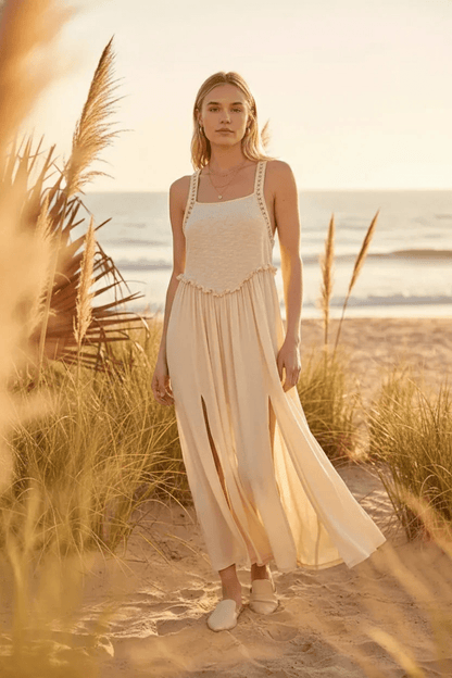 Woman in a flowing dress standing on a beach with grasses in the foreground