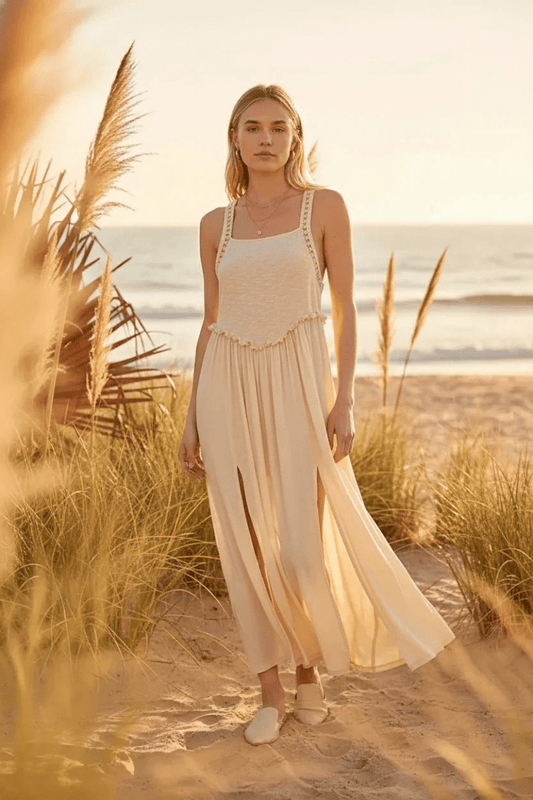 Woman in a flowing dress standing on a beach with grasses in the foreground