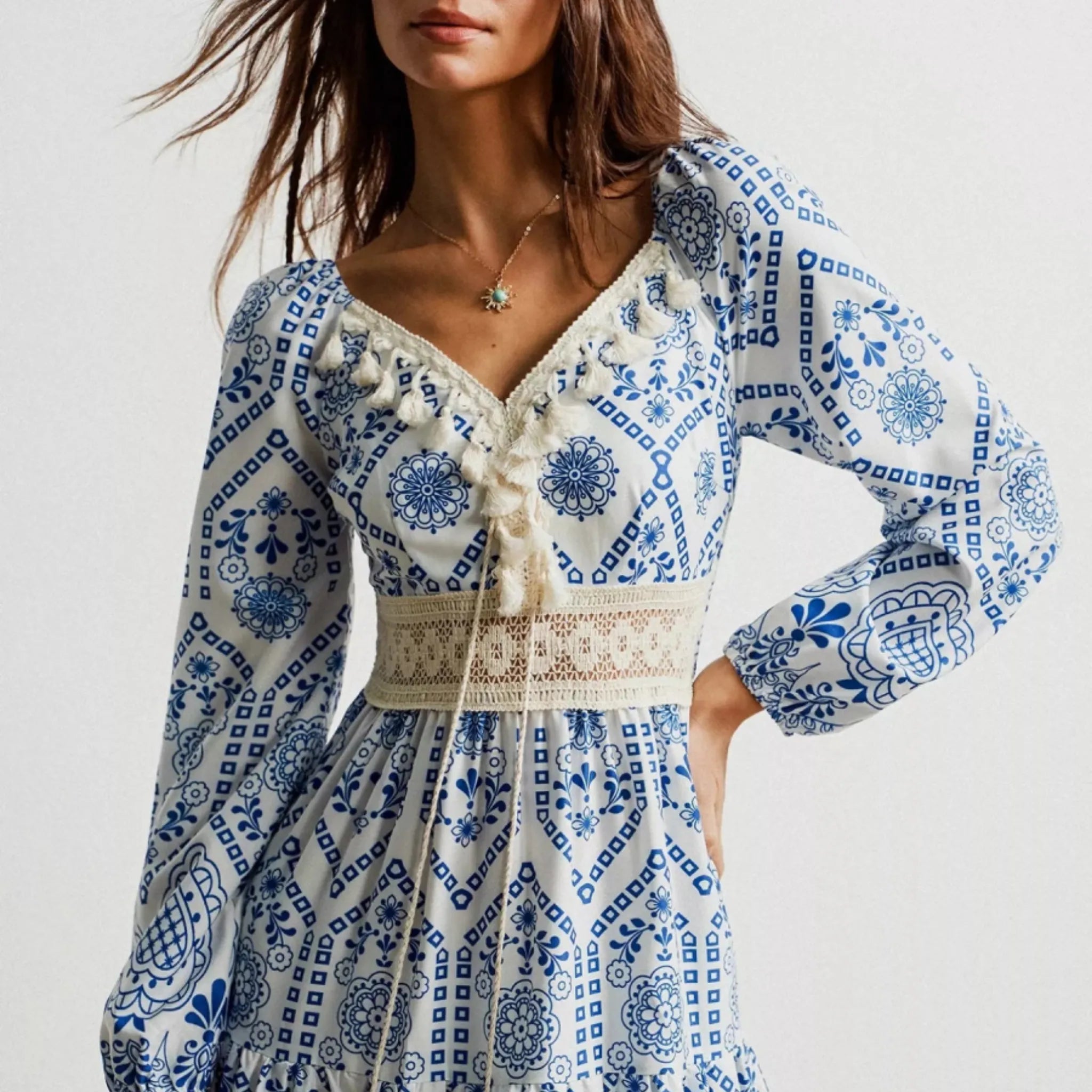 Woman wearing a blue and white patterned dress with long sleeves on a plain background