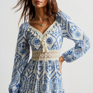 Woman wearing a blue and white patterned dress with long sleeves on a plain background