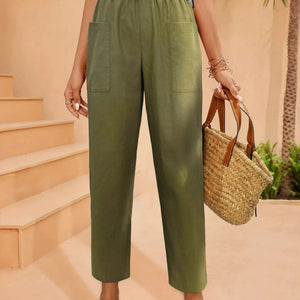 Person wearing green pants holding a straw bag on a peach-colored background