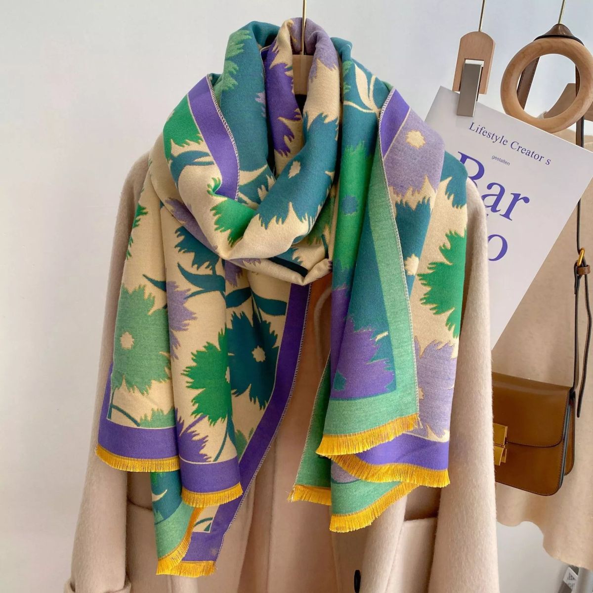 Colorful patterned scarf with green, purple, and yellow on a wooden hanger against a white background.