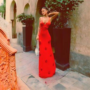 Woman in a red dress standing in an outdoor setting with plants and architectural elements.