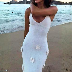 Woman in a white dress with floral details standing on a beach.