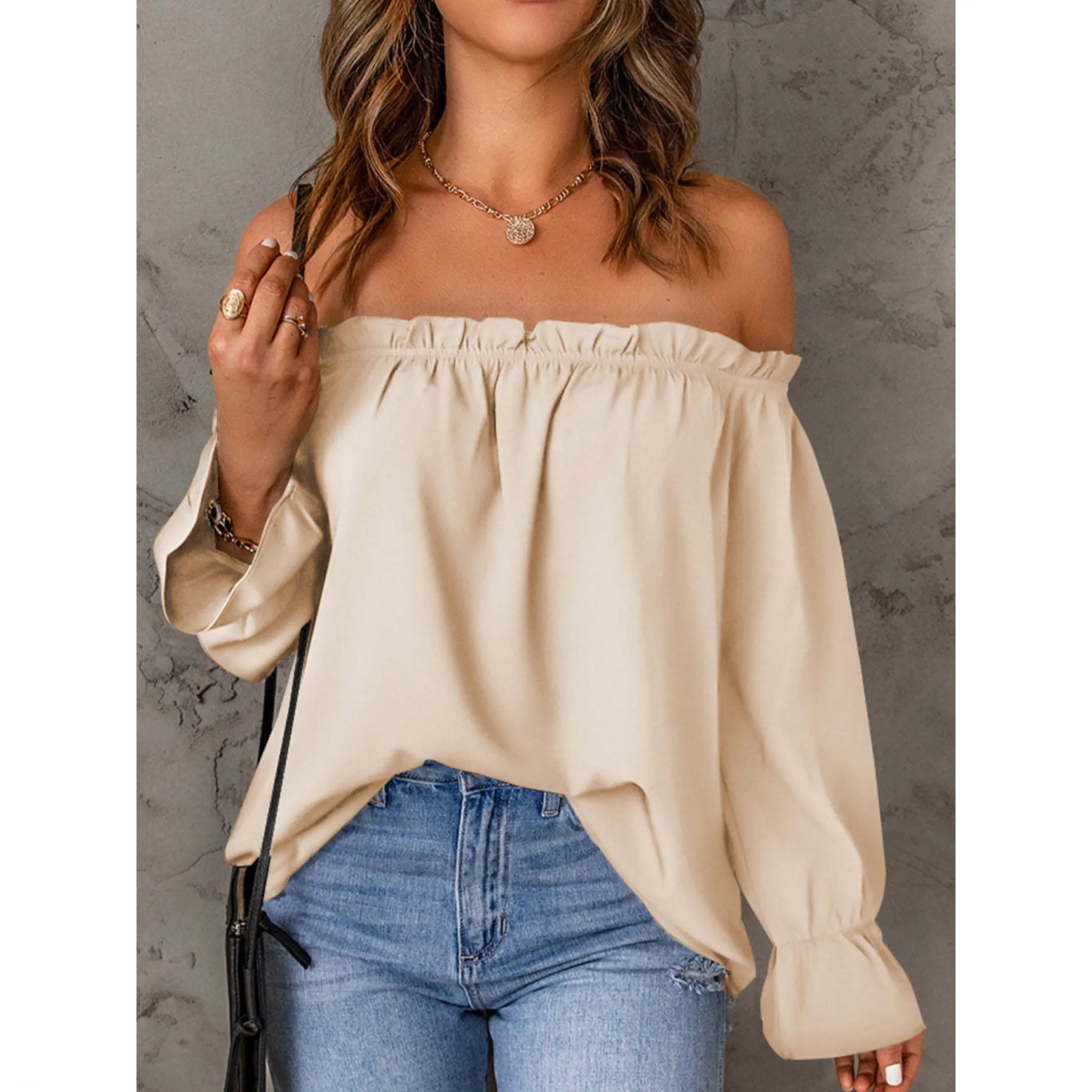 Woman wearing a beige off-shoulder top and blue jeans against a gray background