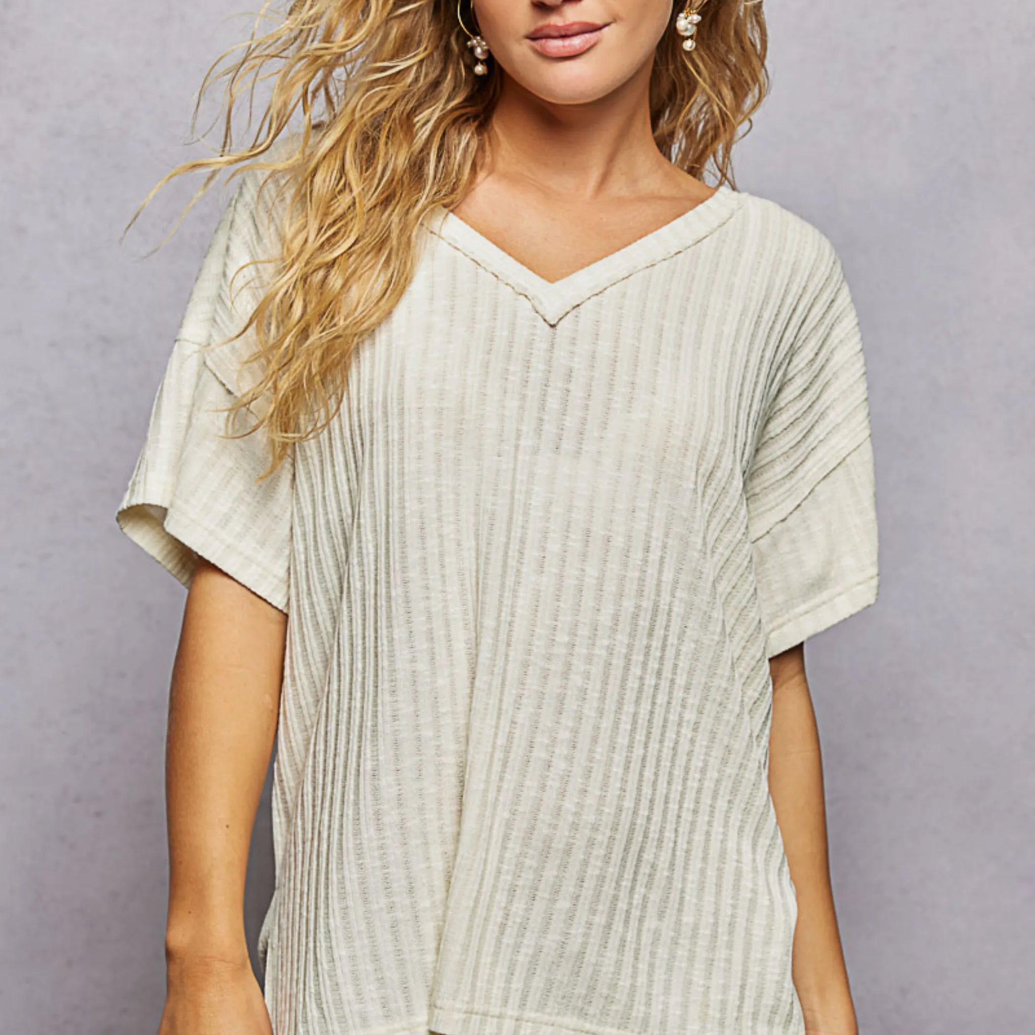 Woman wearing a light-colored ribbed top against a gray background