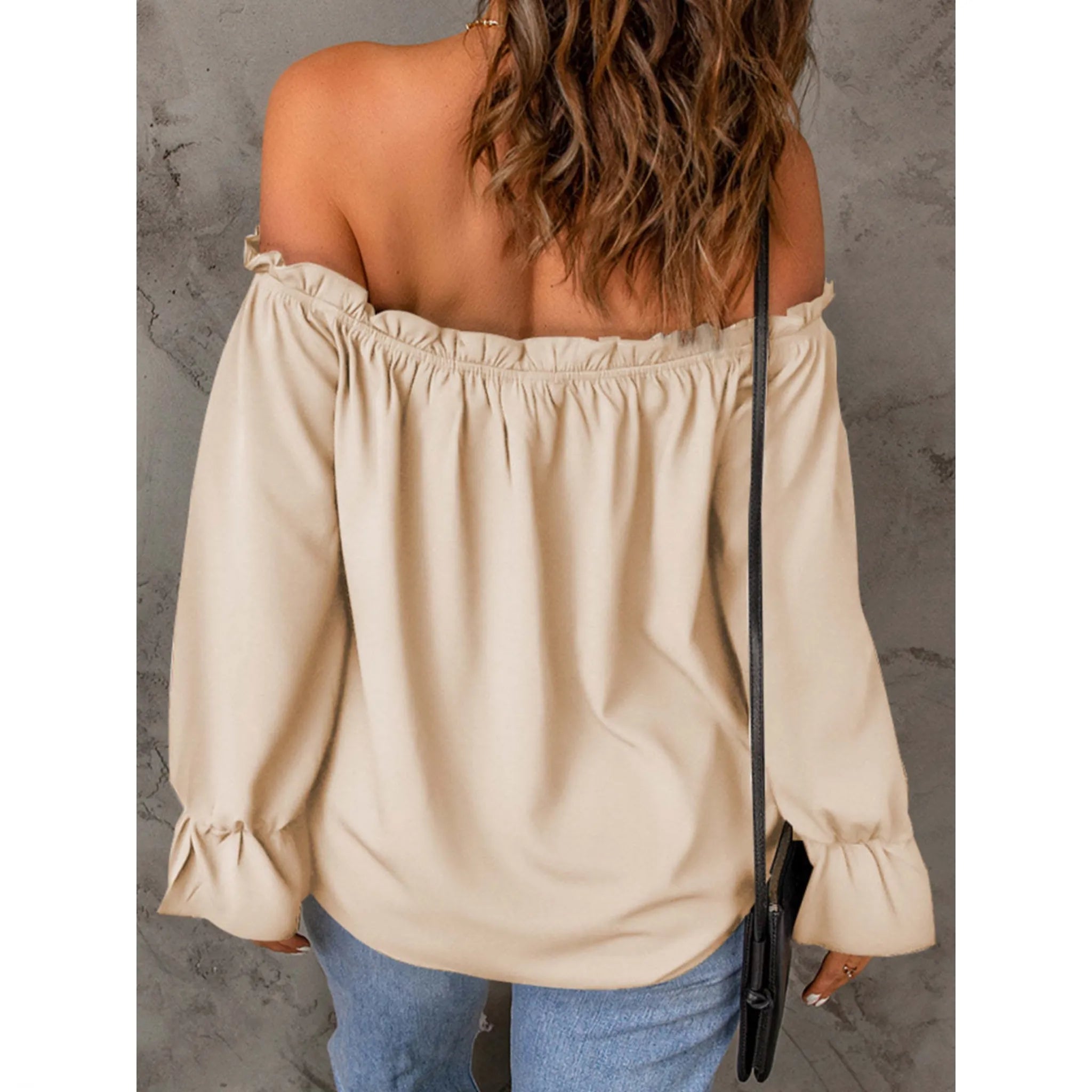 Beige off-shoulder top worn by a person against a gray concrete wall.