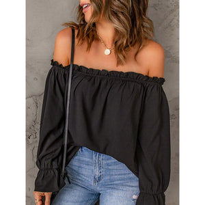 Woman wearing a black off-shoulder top and blue jeans against a gray background