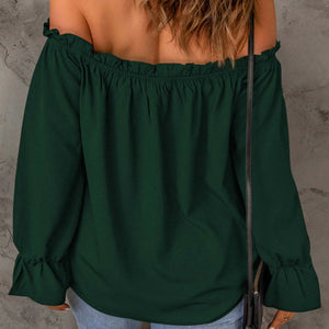 Green off-shoulder blouse worn by a person against a gray concrete wall.