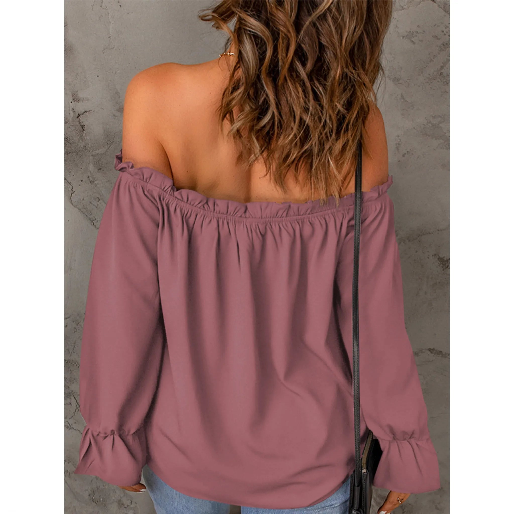 Woman wearing a mauve off-shoulder blouse against a gray concrete wall.