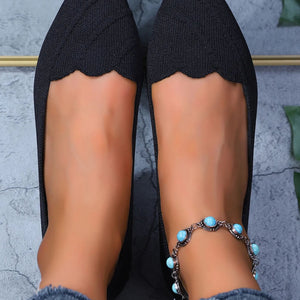 Black flats worn with turquoise beaded anklets on a neutral background